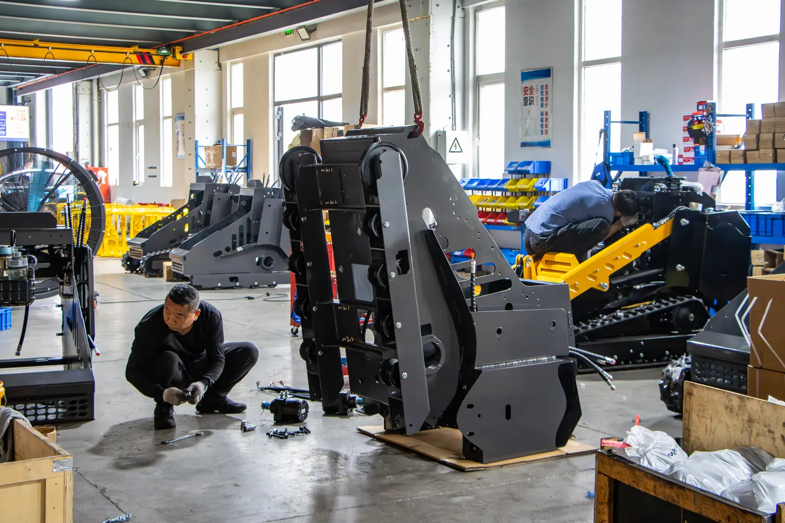 Technicians assembling a black tracked loader frame on the assembly floor