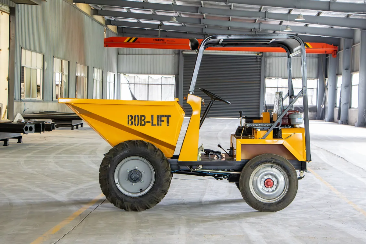 A yellow wheeled mini dumper with an open canopy frame and BOB-LIFT on the hopper, side view, in a large empty hall