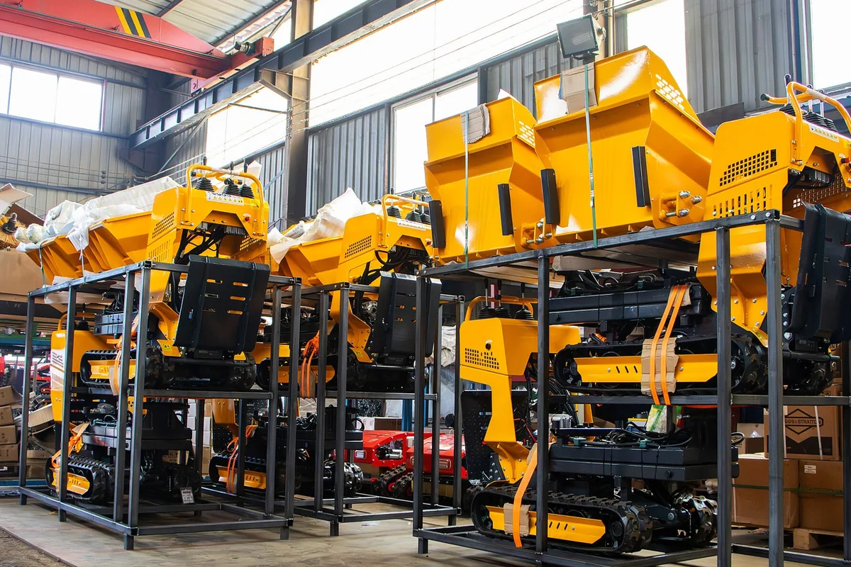 Yellow tracked mini dumpers strapped on black steel racks, two tiers high, in a factory hall