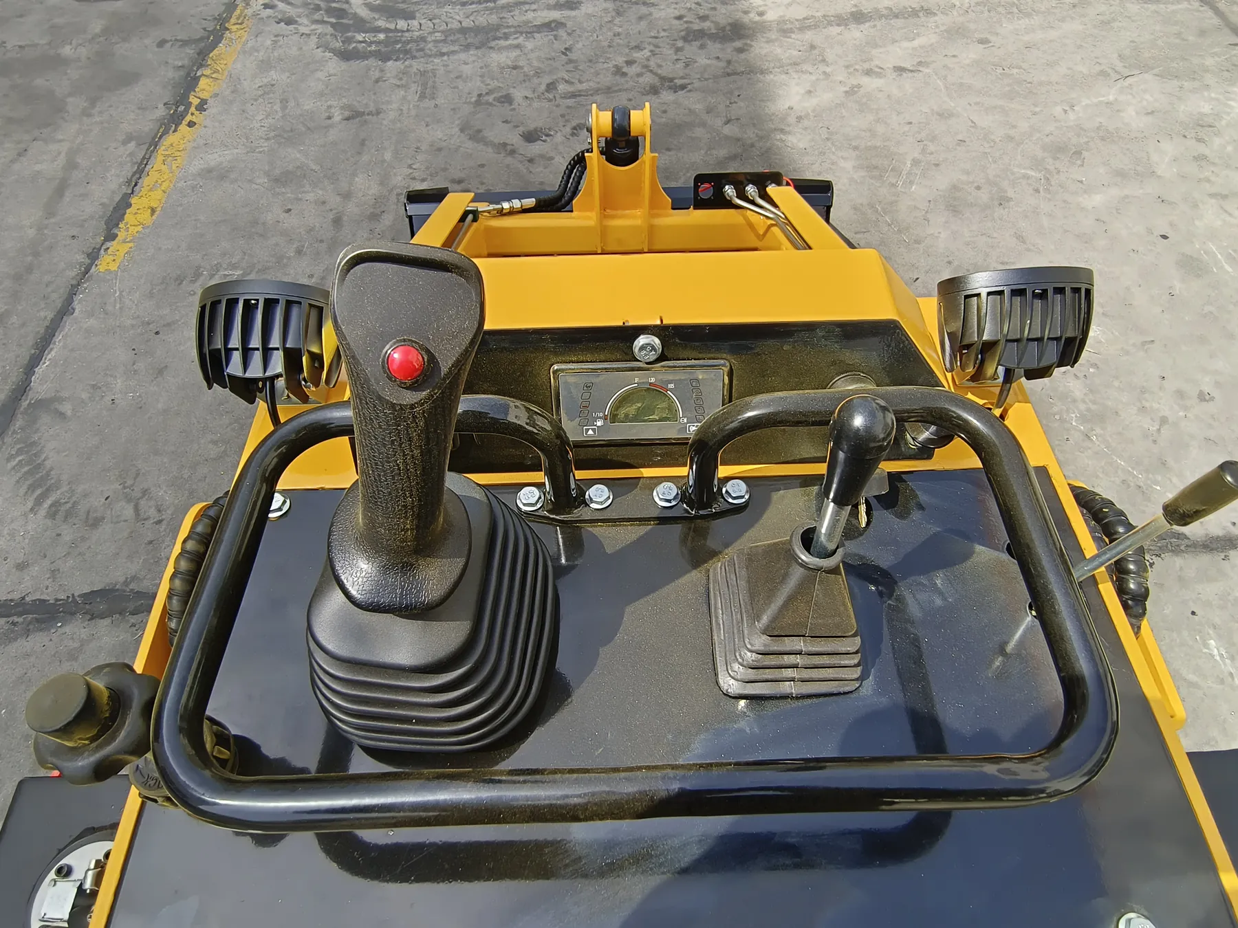 View from the stand-on platform of a yellow BL-S750-H: a joystick with a red button, a second control lever, a gauge and a curved grab handle around the control panel