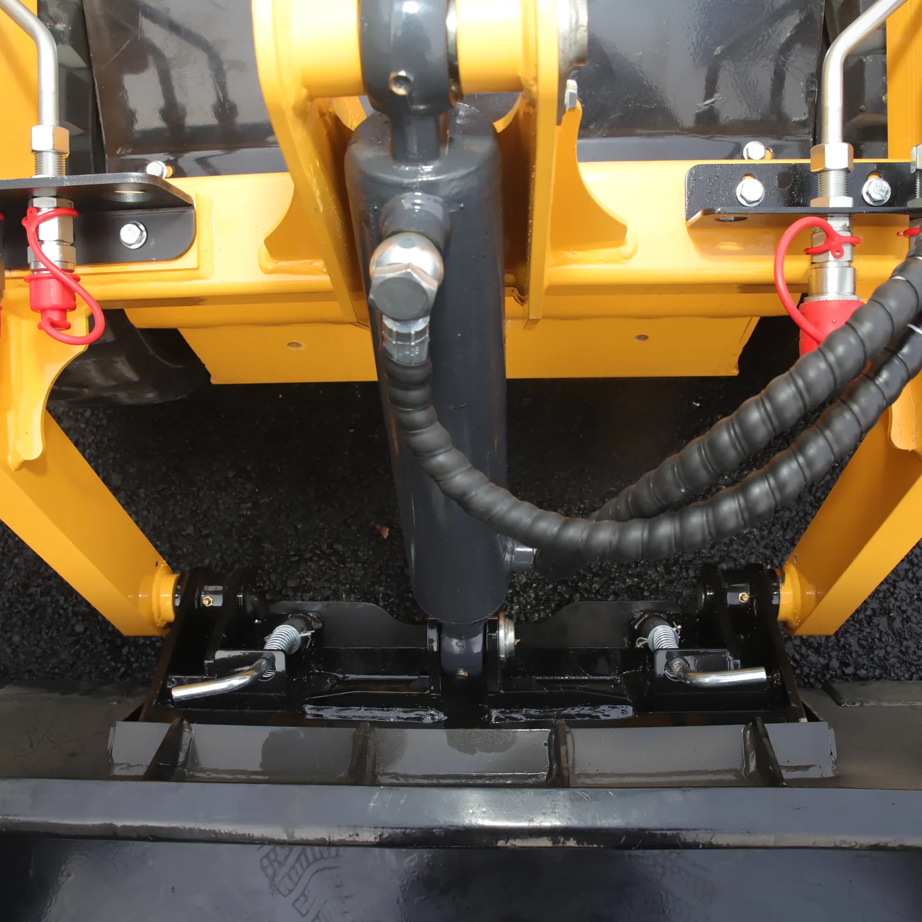 Close-up of the quick-attach plate on a yellow BL-S750-H, with two locking levers holding a black bucket and red-capped auxiliary hydraulic couplers on either side