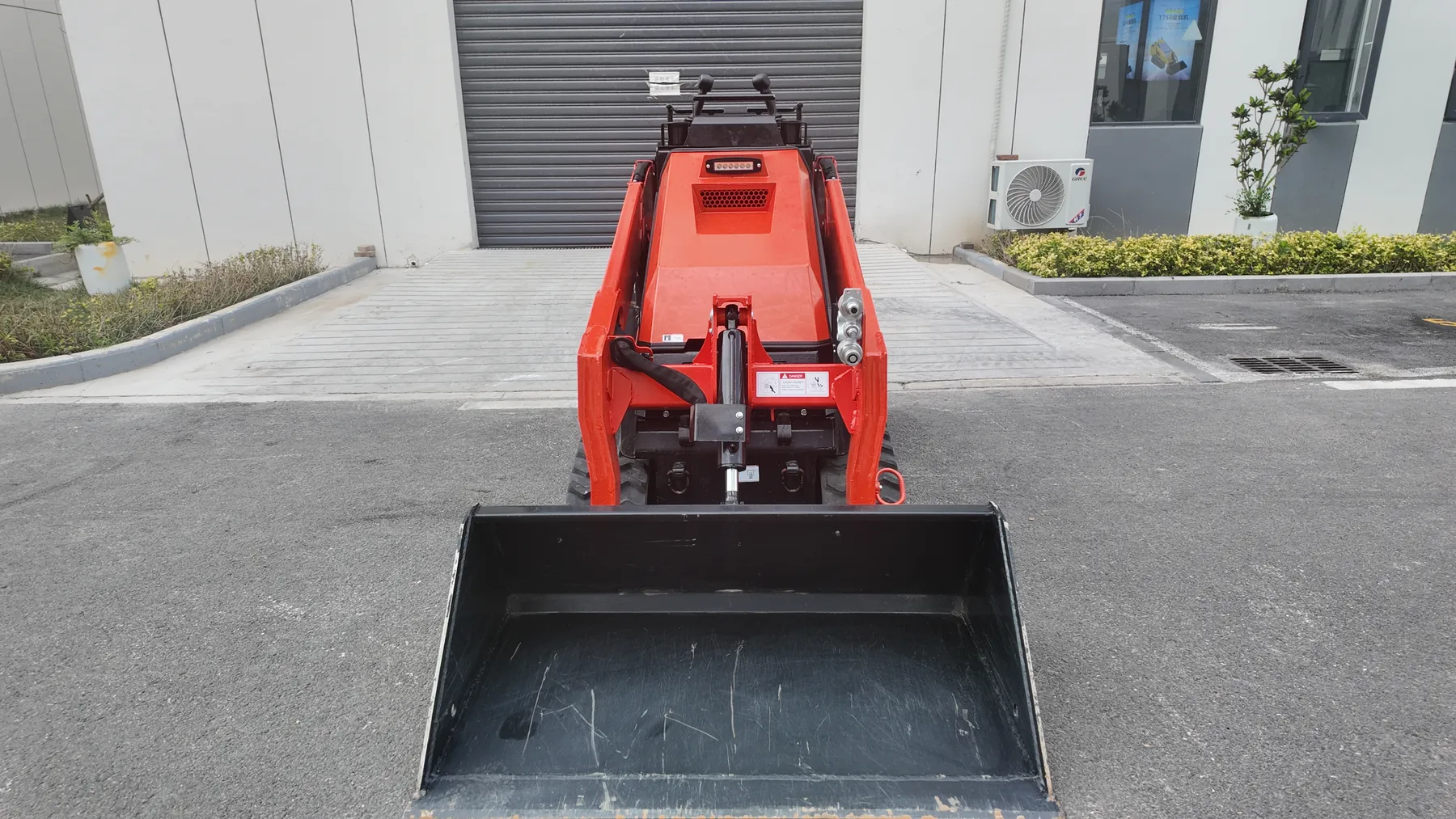Front view of a red BL-T1000-H tracked mini skid steer with its black bucket lowered, the bucket visibly wider than the machine body behind it
