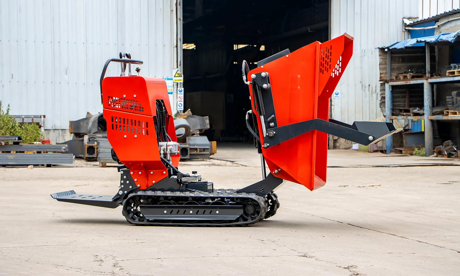 Red BL-T500-HD tracked mini dumper in side view with its hopper tipped fully forward on the lift arms, past upright, beside the handlebar and engine cover